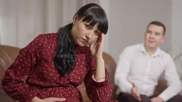 Portrait of Sad Stressed Pregnant Woman Rubbing Temples and Stroking Belly As Blurred Man Yelling