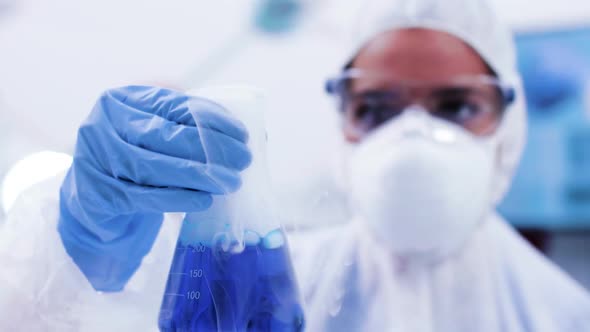 Close Up of Female Scientist in Protection Equipment Holding a Bottle with Smoking Blue Fluid