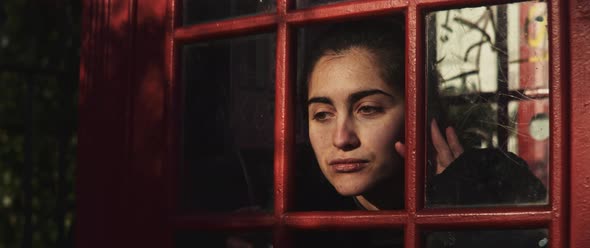 Young woman making silly faces through the window of a phone booth