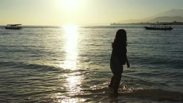 Silhouette of girl washing her feet on warm clear water of sea at sunset moments over lagoon with bo