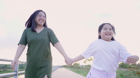 Front view of Asian mom and kid holding hand and running outdoor