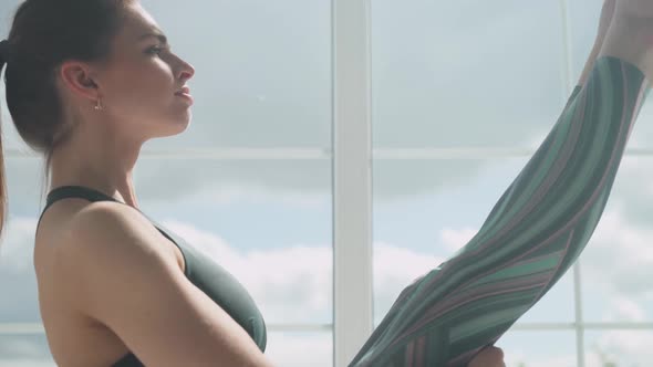 Young Female Doing Yoga in a White Room Filled with Light Performs Yoga Stands Near the Large Window