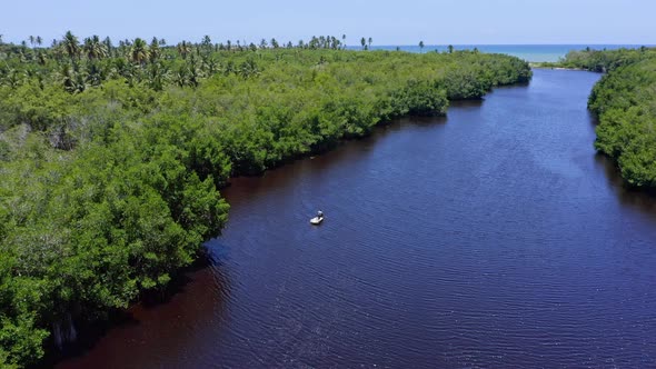 Aerial view of small boat cruising on idyllic river surrounded by mangrove forest during summer - Tr