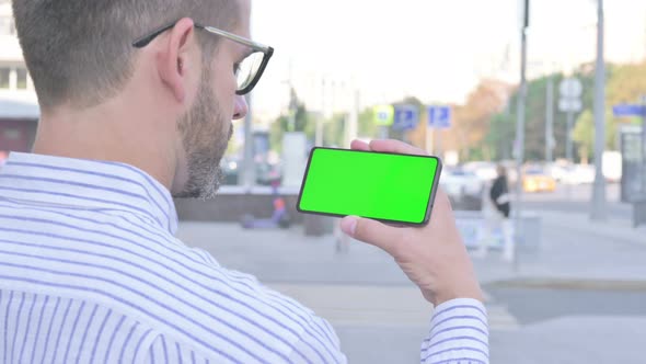 Young Adult Man Holding Horizontal Smartphone with Green Screen Outdoor