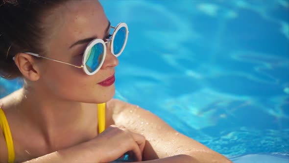 Stylish Attractive Woman in Yellow Swimsuit and Sunglasses in the Swimming Pool