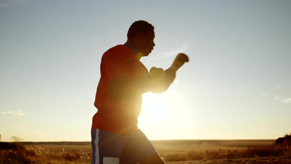 Black Man with Bandaged Fists Boxing Outdoors Training Punches Sunset Background Side View