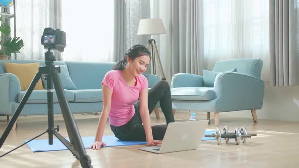 Asian Woman In Sportswear Is Sitting On The Floor Using A Laptop And Shoots Video On Camera At Home