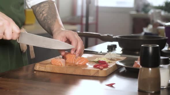 male chef cuts fillet of fresh salmon into large chunks. Cooking fish in kitchen