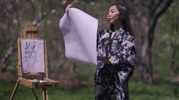 Happy Beautiful Asian Young Woman in Kimono Opening Rolled Picture Admiring Artwork Smiling