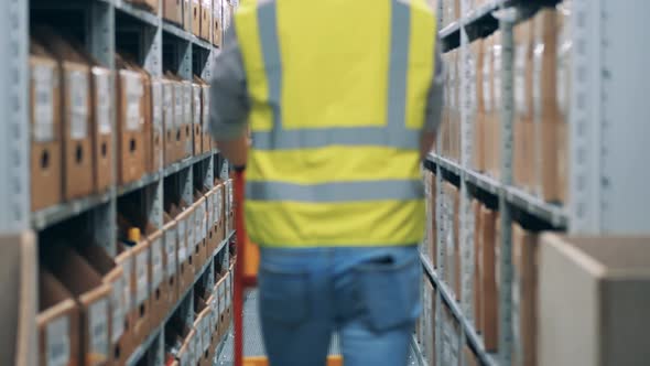 Warehouse Worker is Going Along the Premises with a Trolley