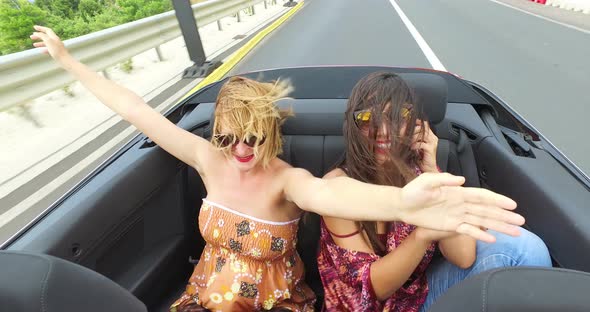 Two beautiful young women raising their arms up while riding in convertible