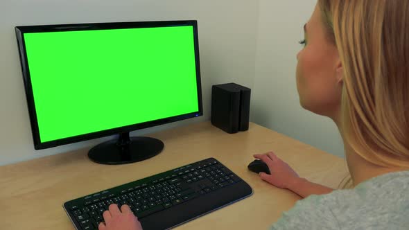 A Young Woman Sits at a Desk and Works on a Computer with a Green Screen