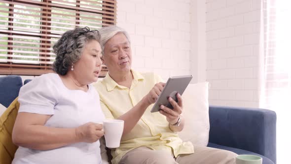 Asian elderly couple using tablet and drinking coffee in living room at home