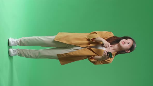 Full Body Of Young Asian Woman Emotionally With Phone While Standing In The Green Screen Studio