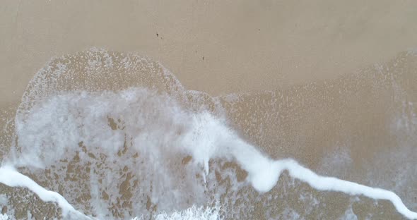 Static top down view of tropical beach, foamy ocean waves washing sand.