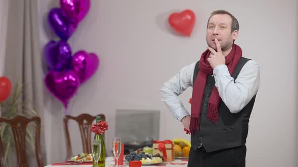 Thoughtful Handsome Caucasian Man Standing at Home at Decorated Valentine's Table with Champagne
