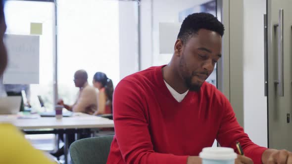 African american male and female business colleagues talking and taking notes in office