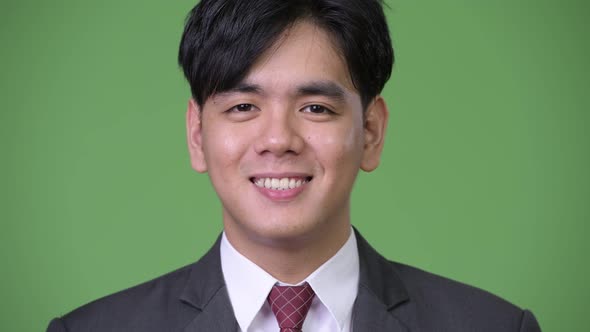 Happy Young Handsome Asian Businessman Smiling Against Green Background