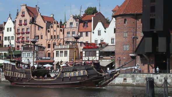 Pirate-like tourist sailing ship moving along waterfront of old medieval city