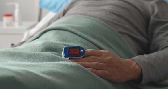 Close Up of Patient Lying in Hospital Bed Wearing Pulse Oximeter to Measure Blood Oxygen Saturation