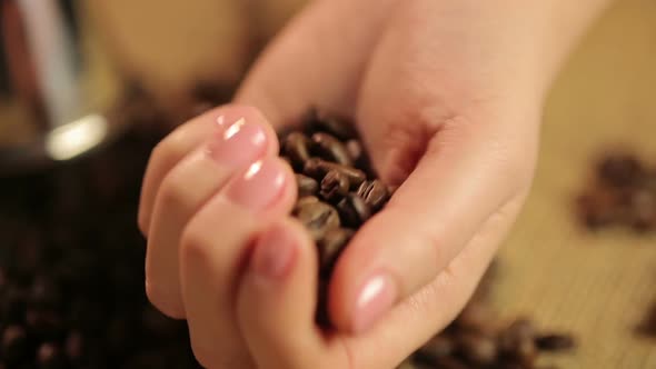 Woman's hand touching roasted coffee beans, preparing to enjoy strong taste