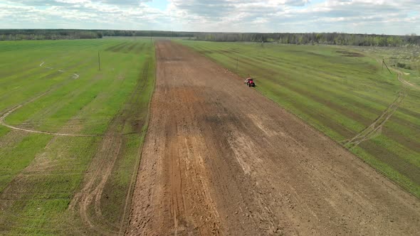 Tractor on the Background of a Rich Cloudy Sky in Sunny Weather. Soil Treatment Before Planting