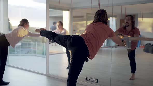 People practicing yoga in Warrior pose near barre