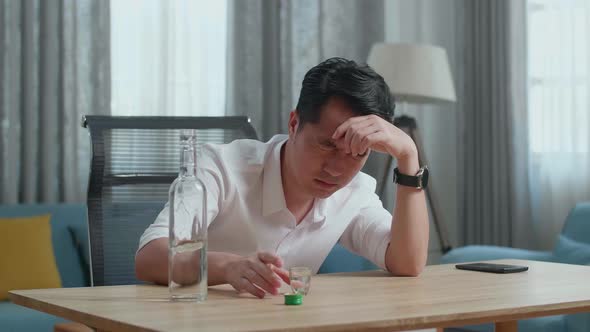 Drunk, Depressed Asian Man Pouring Vodka In A Shot Glass Before Drinking And Using A Fist Smashing