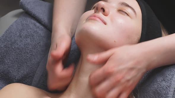 Attractive Woman in a Beauty Salon Lies on the Bed and Receives a Massage on the Neck and Decollete