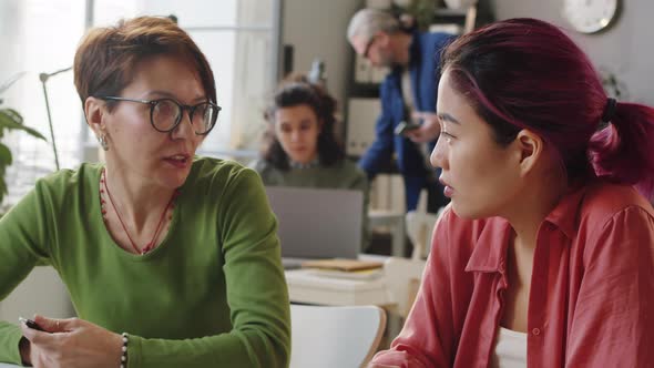Female Mentor Working with Young Asian Trainee in Office
