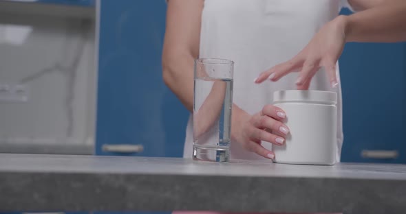A Woman's Hand Opens a White Jar Pours Bcaa Into a Glass and Stirs It