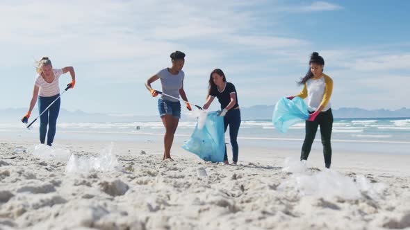 Diverse group of female friends putting rubbish in refuse sacks at the beach