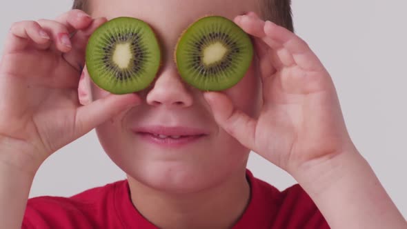 Young boy holding kiwi fruit over eyes