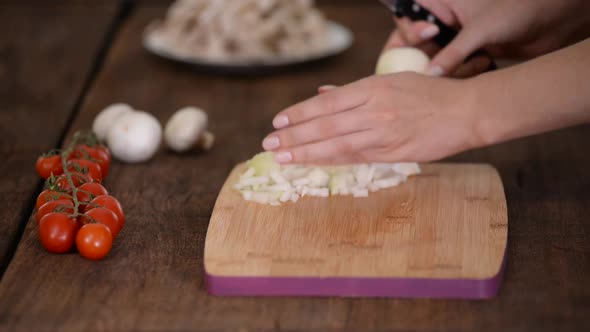 Chef's hands with knife cutting the onion on the wooden board.