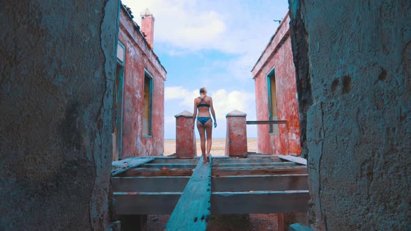 Girl in bikini walking over wooden plank in abandoned lighthouse