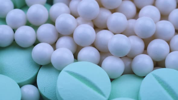 White Round Small Granules Lie Among Green Pills and Rotate Closeup