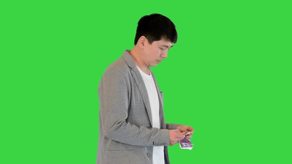 Young Asian Man Counts Money and Puts Them Into Pocket on a Green Screen Chroma Key