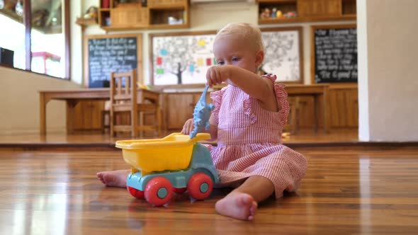 Caucasian Toddler Girl Playing with Toy Car and Dinosaur at Nursery