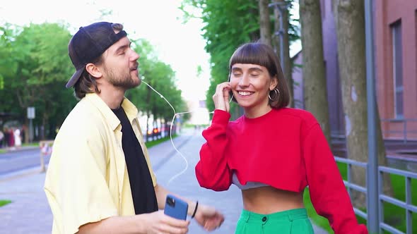 Cute Millenial Couple Dancing on Street Using Phone and Headphones