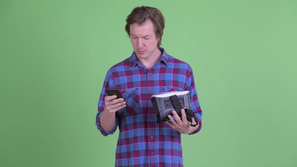 Happy Young Hipster Man Using Phone While Holding Virtual Reality Headset