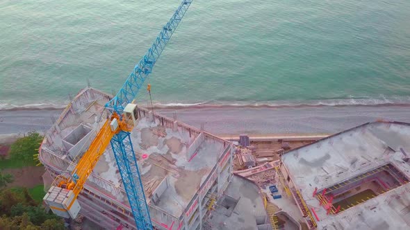crane is working on construction site view from a drone on background of sea.