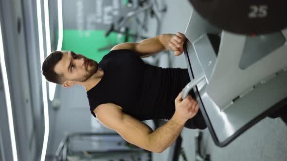 Verical Shot of Man Puts Additional Weights on a Barbell and Doing Leg Exercises