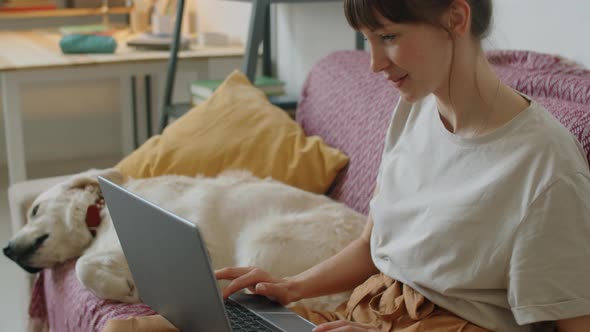 Woman Using Laptop and Petting Dog on Sofa