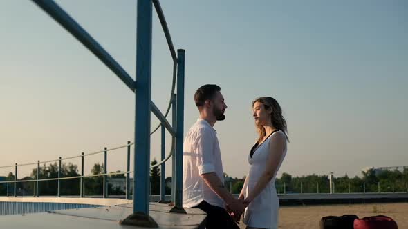 Young Caucasian lovers woman and man are standing on roof  sunset in summer