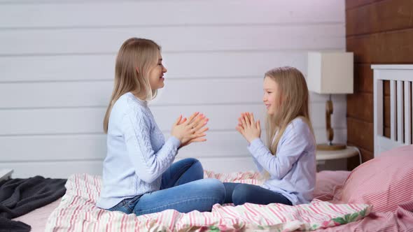 Full Shot Casual Mother and Cute Baby Daugher Enjoying Fooling Clapping Hands Sitting on Bed