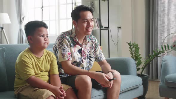 Asian Father And His Son Are Watching Tv While Spending Time Together At Home