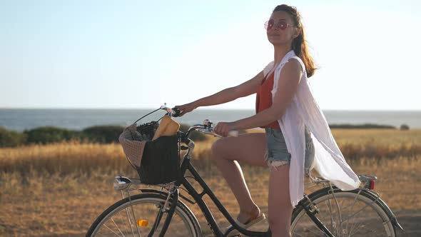 Side View Slim Young Caucasian Woman with Bicycle Looking Away Holding Hand at Forehead Smiling