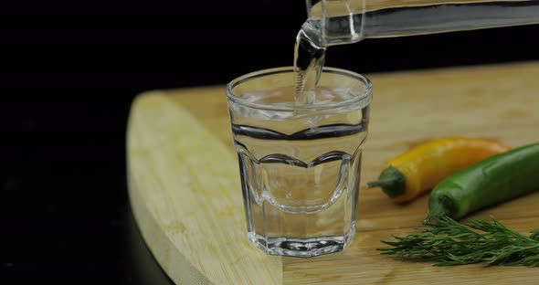 Pour Alcohol Vodka From a Bottle in Shot Glass on Cutting Board with Hot Pepper