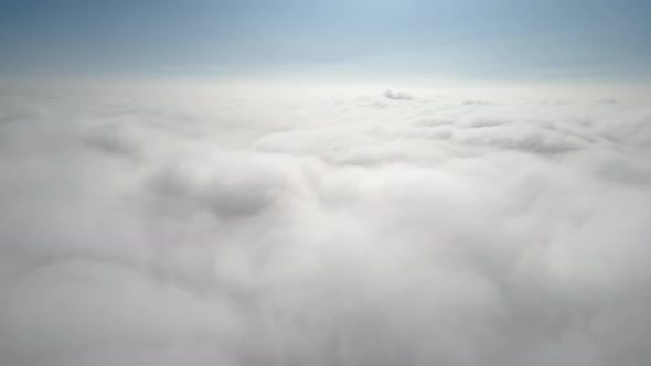 Aerial shot of flying over a layer of soft clouds at dawn