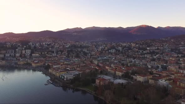 A drone view of a beautiful city surrounded by mountains, next to a lake, during a sunset in autumn.